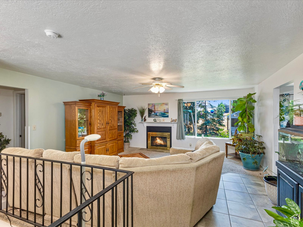 Living room with a ceiling fan, a glass covered fireplace, a textured ceiling, and light tile patterned floors
