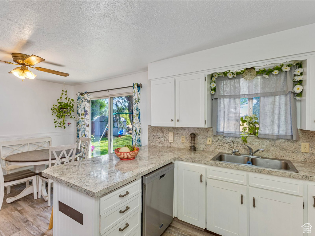 Kitchen featuring dishwasher, light countertops, a peninsula, white cabinets, and decorative backsplash
