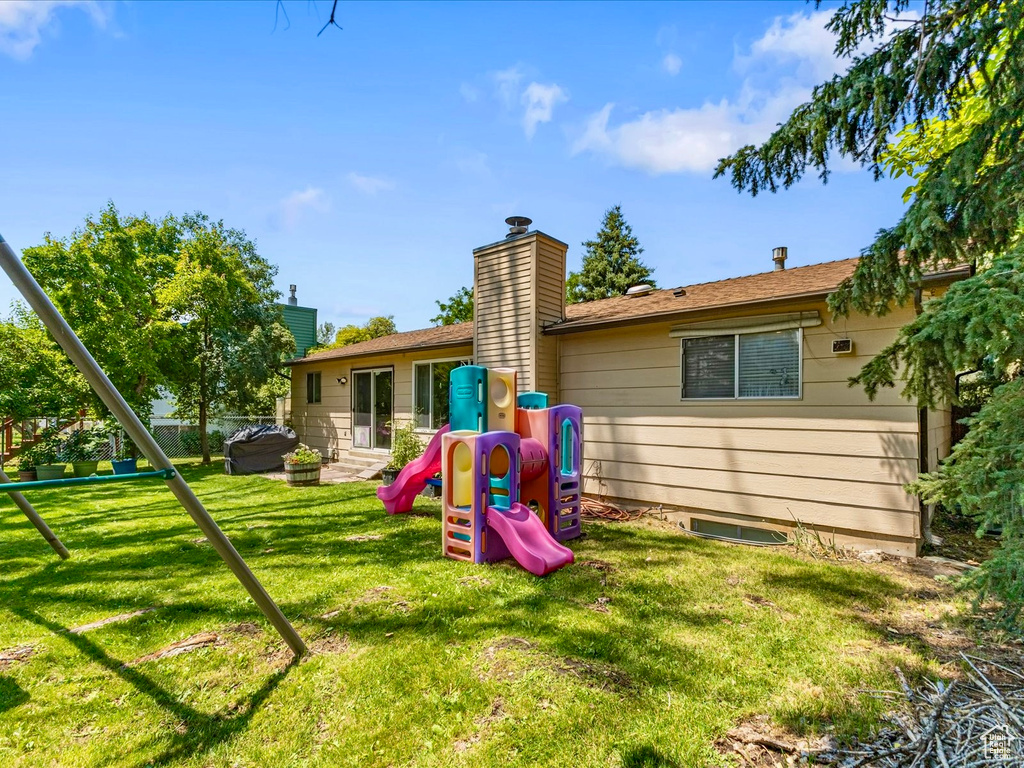 Rear view of property featuring a playground, a yard, and a chimney