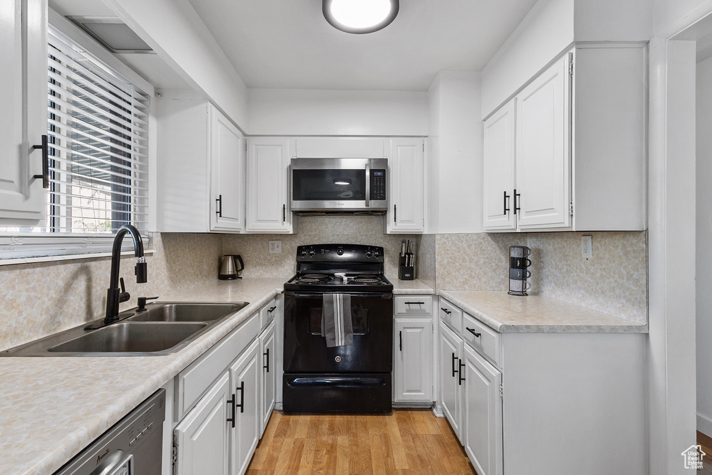 Kitchen with stainless steel appliances, white cabinets, light wood-style floors, tasteful backsplash, and light countertops