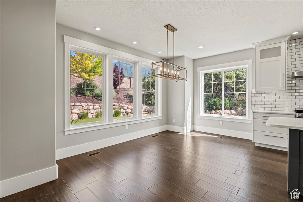 Unfurnished dining area featuring a chandelier, a textured ceiling, recessed lighting, and dark wood-style flooring