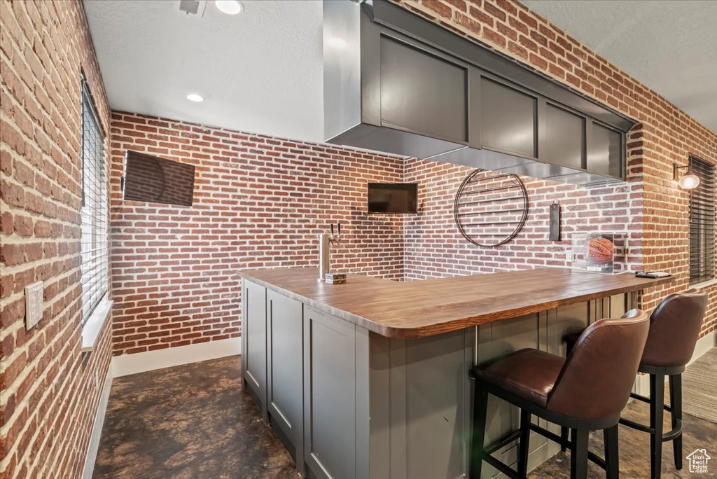 Kitchen with brick wall, a kitchen breakfast bar, a textured ceiling, gray cabinetry, and recessed lighting