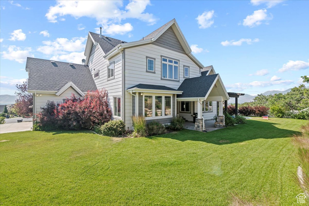 Rear view of property with a lawn, roof with shingles, and a patio area