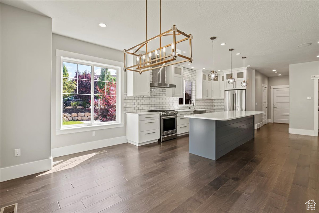 Kitchen with appliances with stainless steel finishes, wall chimney exhaust hood, light countertops, dark wood-type flooring, and recessed lighting