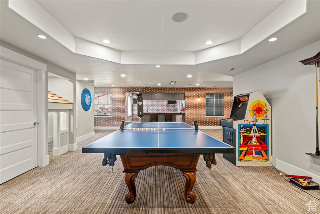 Recreation room featuring recessed lighting, brick wall, carpet, and a raised ceiling