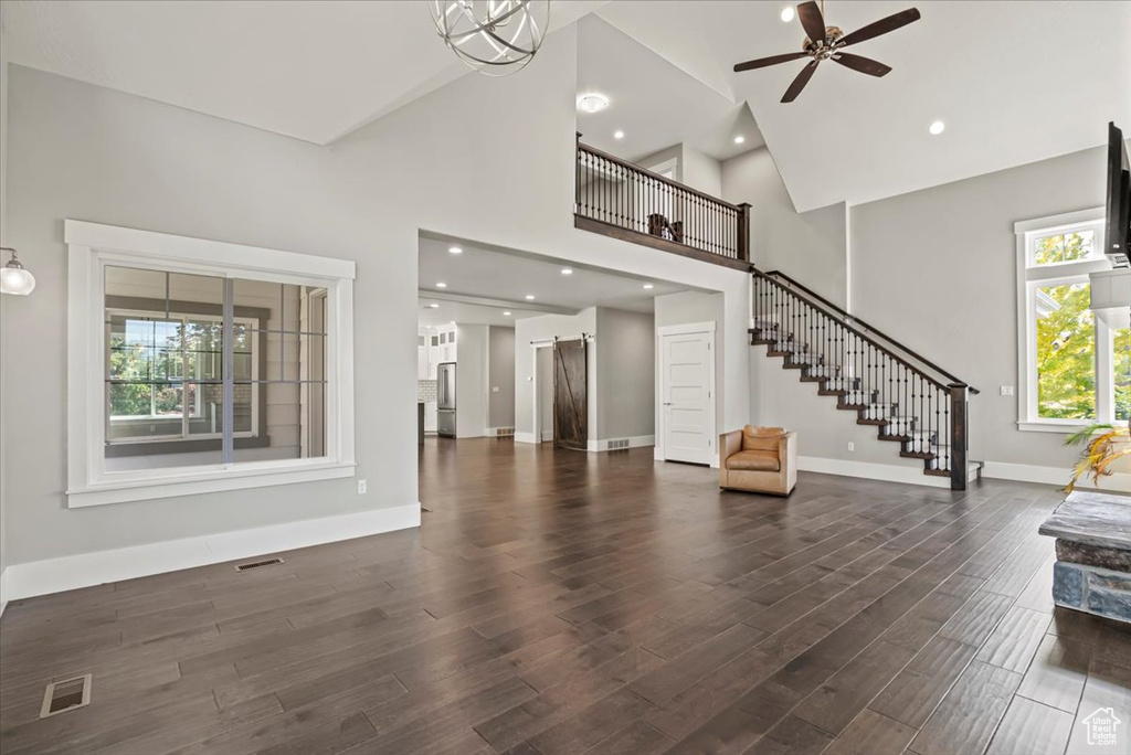 Unfurnished living room featuring high vaulted ceiling, ceiling fan, stairs, and dark wood-type flooring