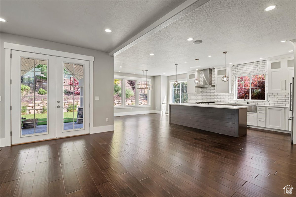Kitchen with wall chimney range hood, white cabinetry, glass insert cabinets, light countertops, and french doors