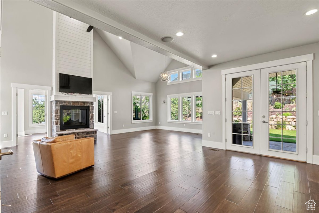 Unfurnished living room featuring french doors, beam ceiling, plenty of natural light, dark wood-type flooring, and a glass covered fireplace