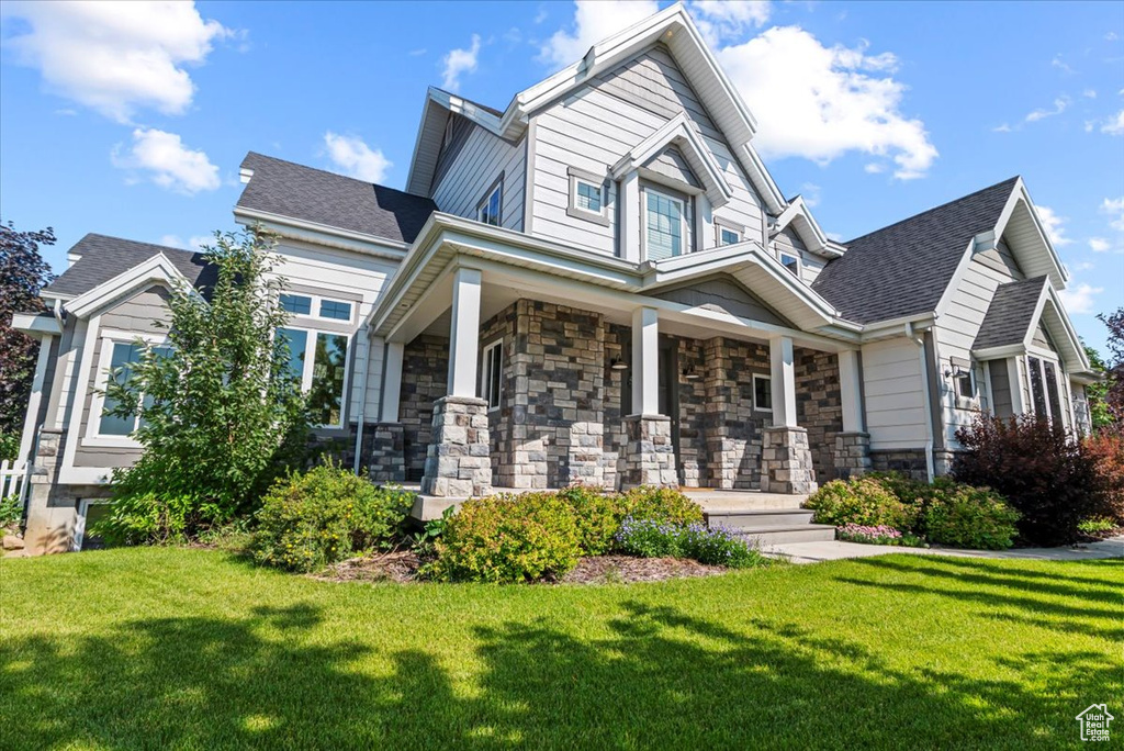 Craftsman-style home featuring a porch, a front lawn, stone siding, and roof with shingles