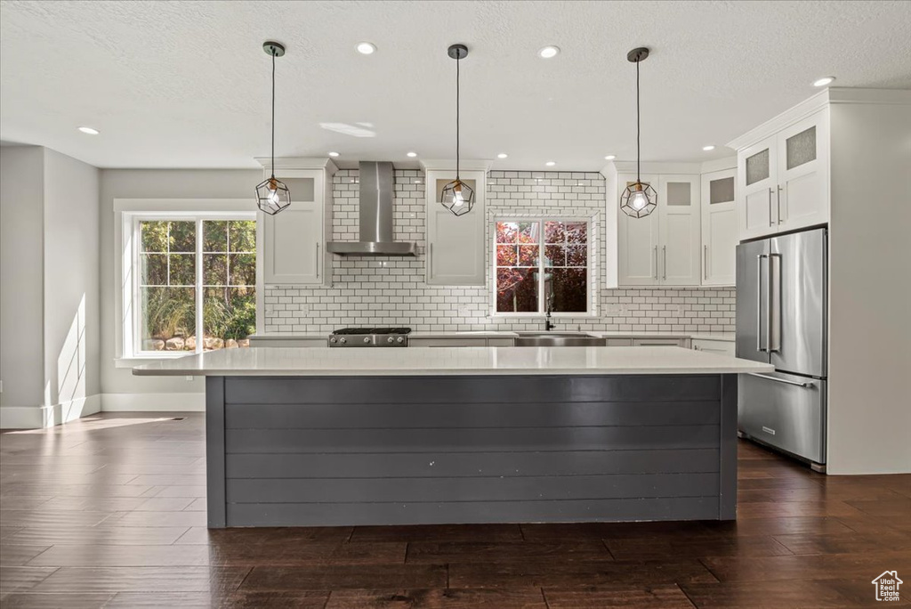 Kitchen featuring wall chimney range hood, high end refrigerator, light countertops, a kitchen island, and white cabinetry