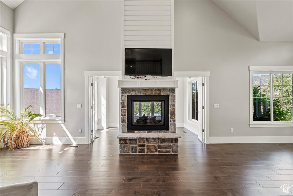 Unfurnished living room with high vaulted ceiling, a stone fireplace, and dark wood-type flooring