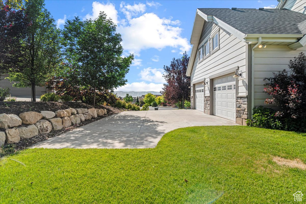 View of grassy yard featuring an attached garage and driveway