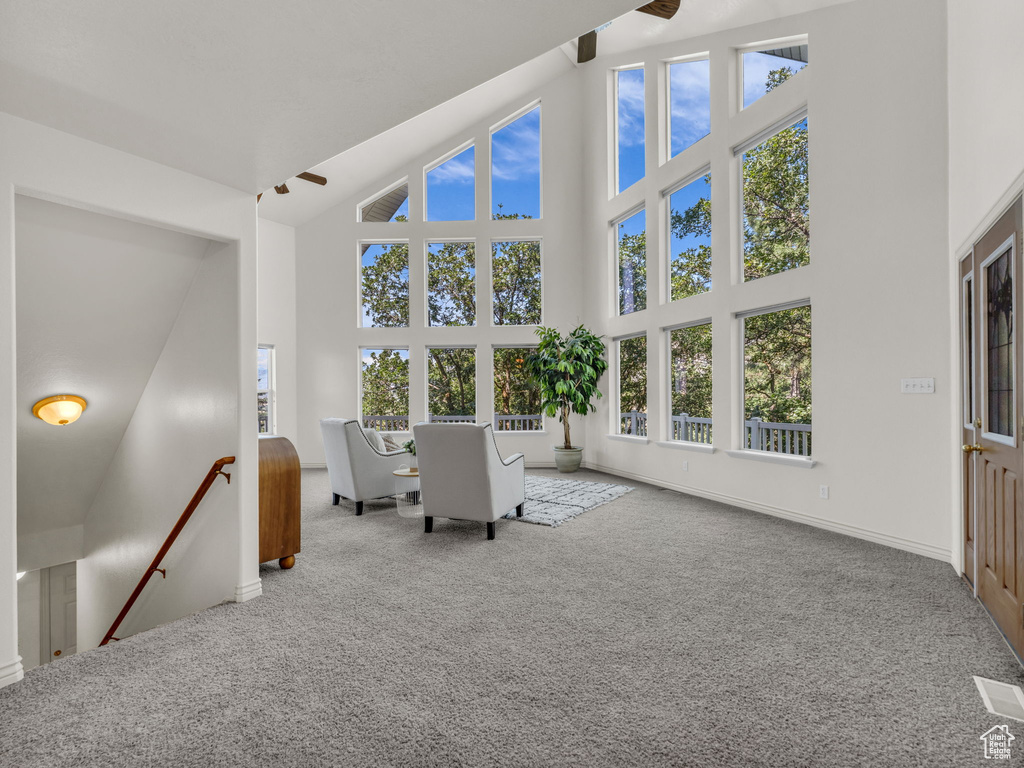 Carpeted living area featuring a ceiling fan and a high ceiling