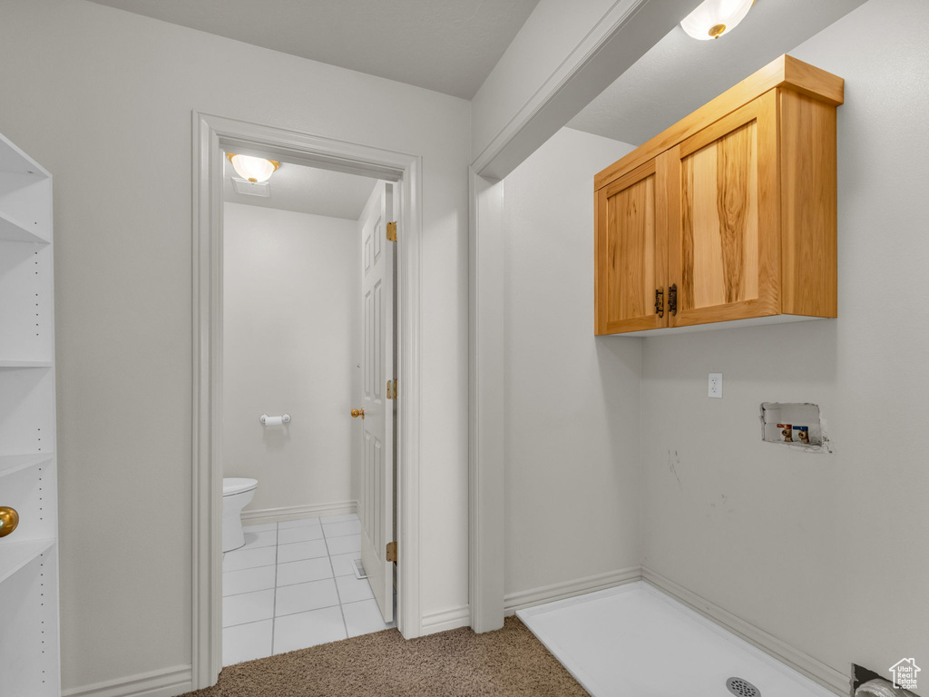 Washroom with cabinet space, washer hookup, light tile patterned floors, and light carpet
