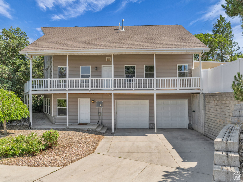 View of front of property featuring an attached garage, concrete driveway, roof with shingles, and covered porch