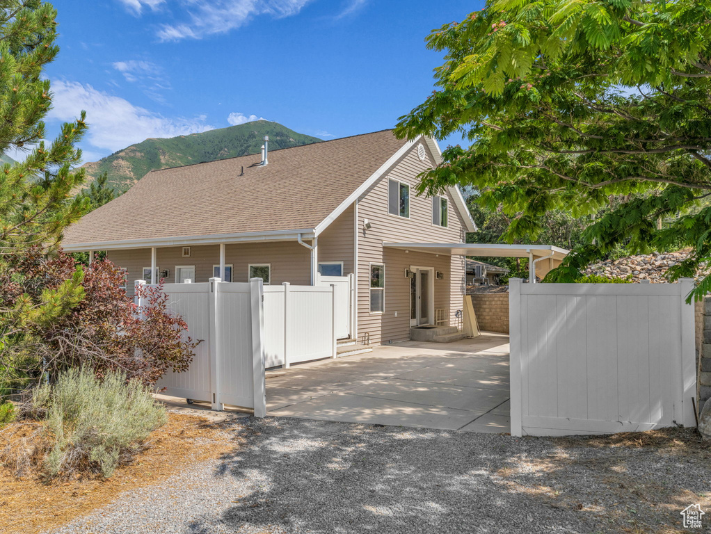 View of property exterior with a mountain view, a shingled roof, driveway, and a patio area