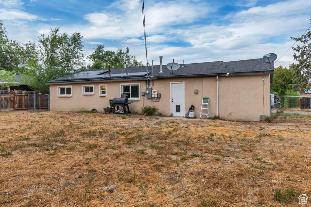Rear view of house featuring stucco siding, a fenced backyard, roof mounted solar panels, and a shingled roof