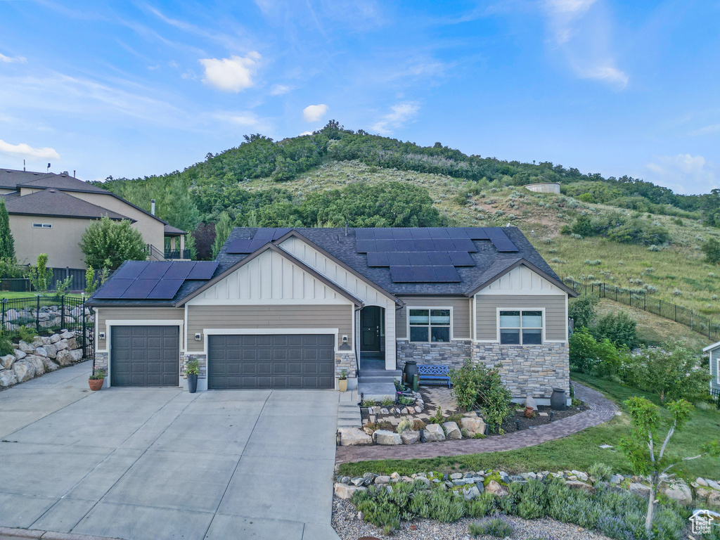 View of front of house with board and batten siding, a garage, concrete driveway, stone siding, and roof mounted solar panels