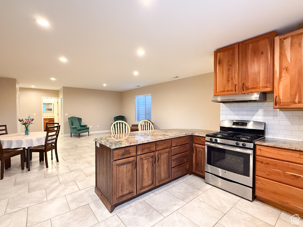 Kitchen featuring stainless steel range with gas cooktop, under cabinet range hood, a peninsula, recessed lighting, and light stone countertops