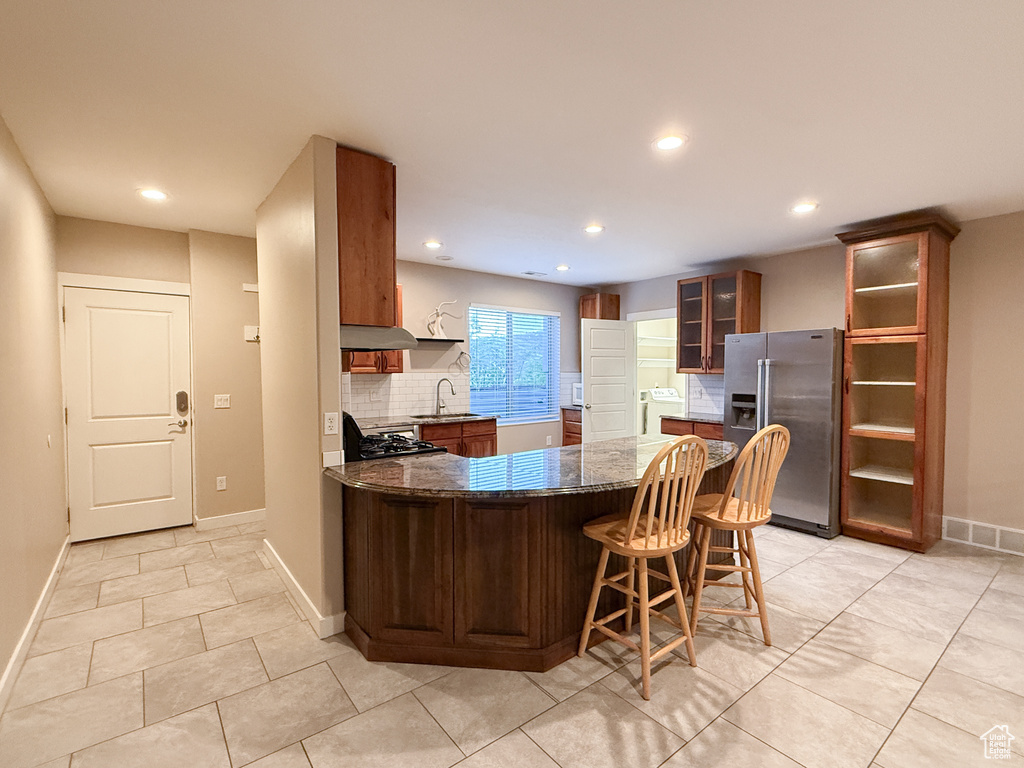 Kitchen featuring stainless steel refrigerator with ice dispenser, a peninsula, recessed lighting, under cabinet range hood, and decorative backsplash