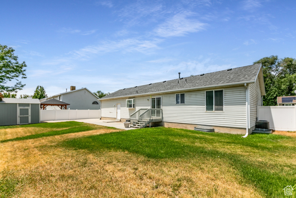 Back of house featuring a fenced backyard, a patio area, a storage shed, and a shingled roof