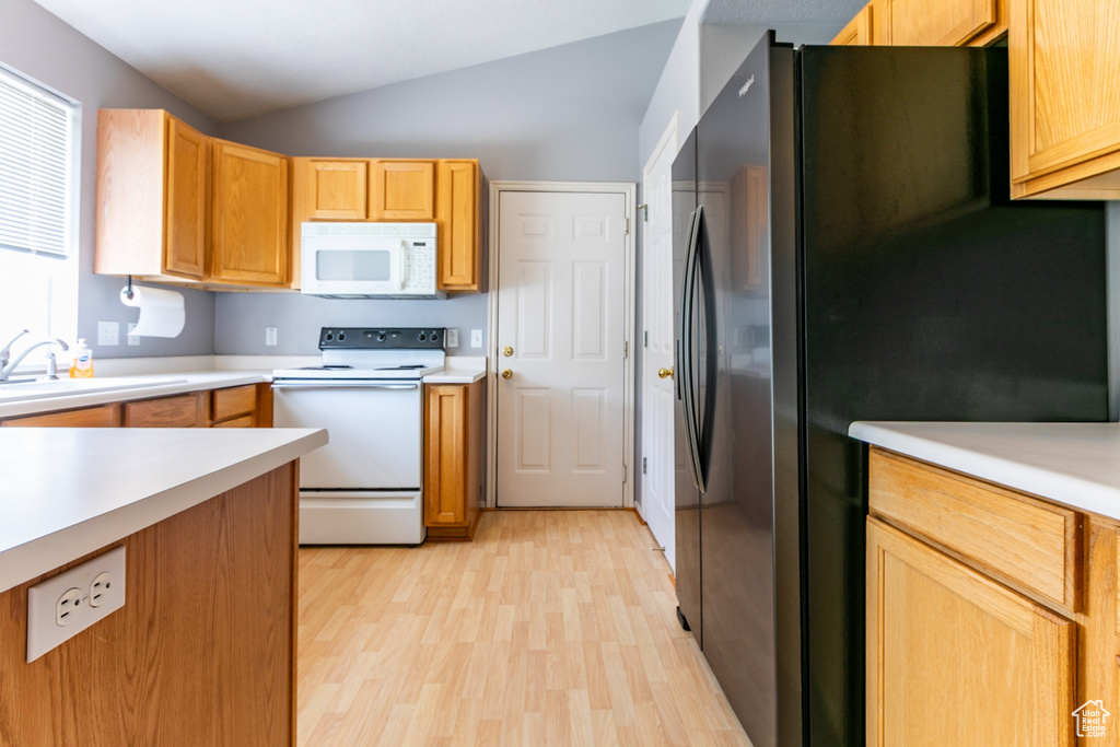 Kitchen with white appliances, vaulted ceiling, light wood-style flooring, and light countertops