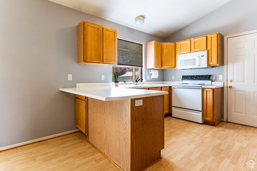 Kitchen featuring white appliances, light wood-style flooring, a peninsula, lofted ceiling, and light countertops