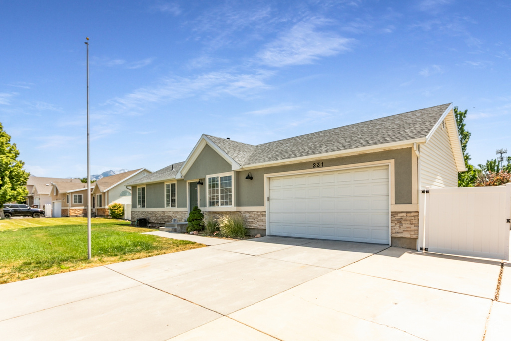 Ranch-style home with concrete driveway, an attached garage, a front lawn, stone siding, and a shingled roof