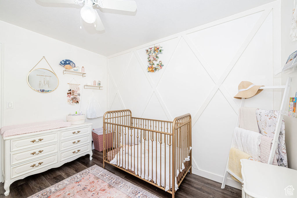 Bedroom featuring dark wood-style floors, a crib, and ceiling fan