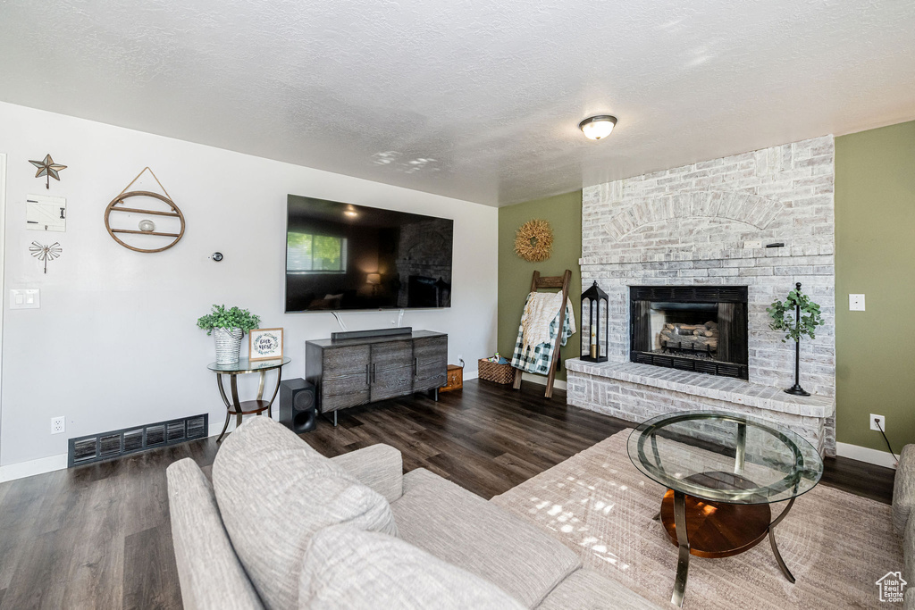 Living area with wood finished floors, a brick fireplace, and a textured ceiling