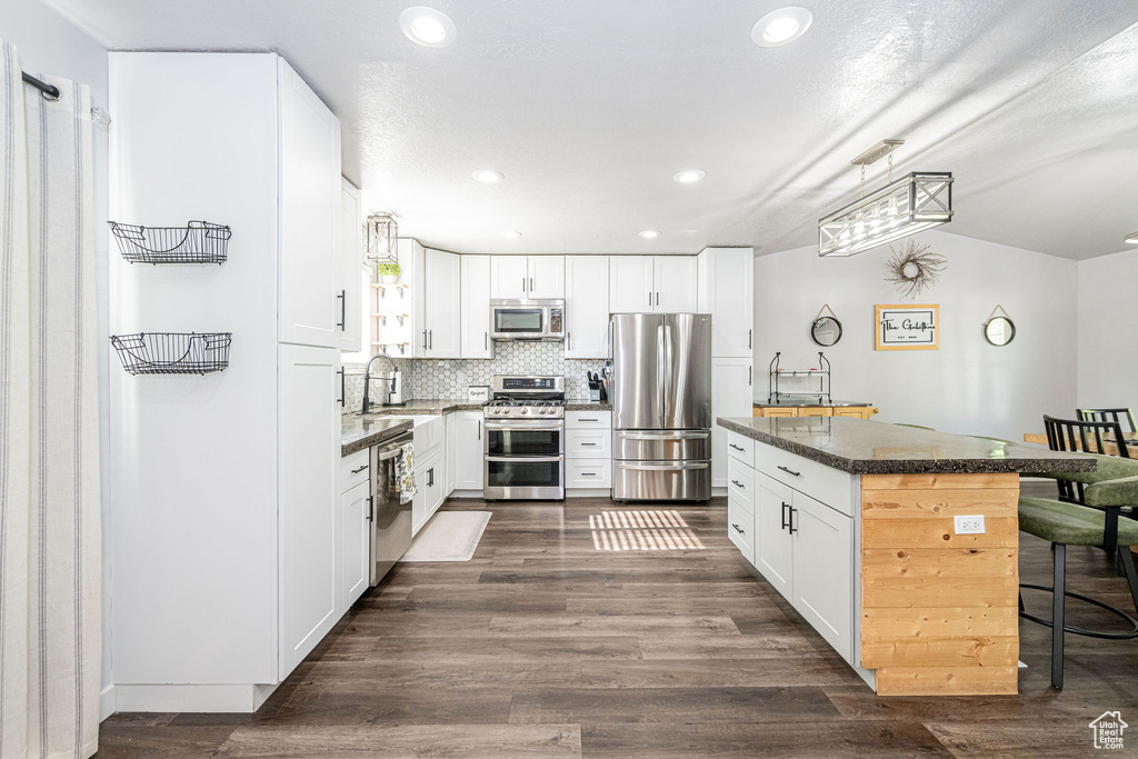Kitchen with stainless steel appliances, a breakfast bar, a kitchen island, recessed lighting, and white cabinets