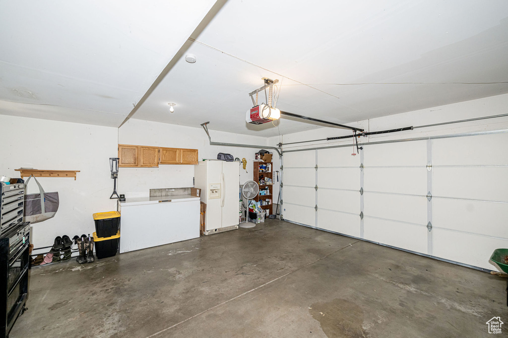 Garage featuring white refrigerator with ice dispenser and a garage door opener