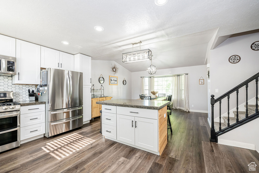 Kitchen featuring stainless steel appliances, lofted ceiling, dark countertops, backsplash, and dark wood finished floors