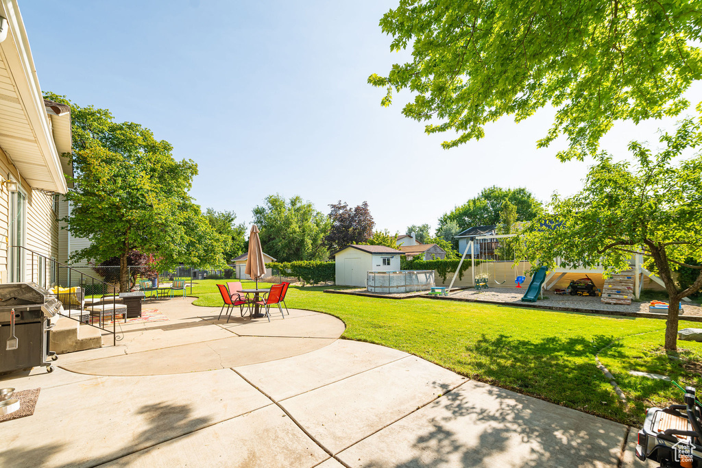 View of patio featuring a storage unit, a playground, area for grilling, outdoor dining space, and a swimming pool