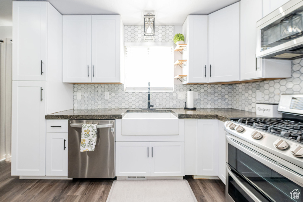 Kitchen with stainless steel appliances, white cabinetry, and dark wood-style flooring