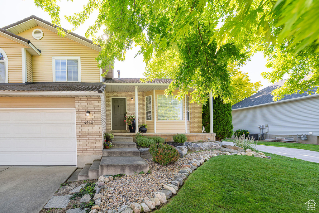 Traditional home featuring brick siding, a garage, concrete driveway, a front lawn, and a porch