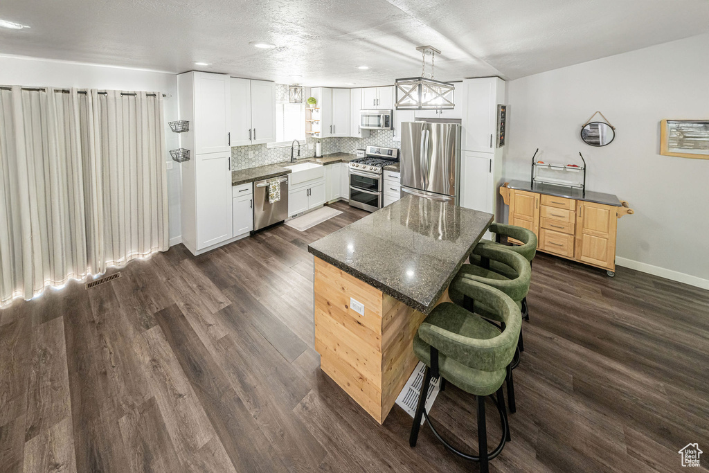 Kitchen with appliances with stainless steel finishes, a kitchen bar, tasteful backsplash, dark wood-style flooring, and a center island