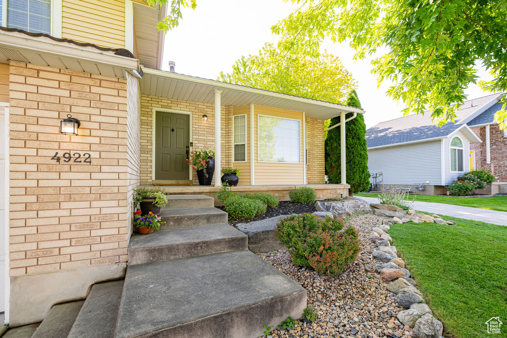 Doorway to property featuring covered porch, brick siding, and a lawn