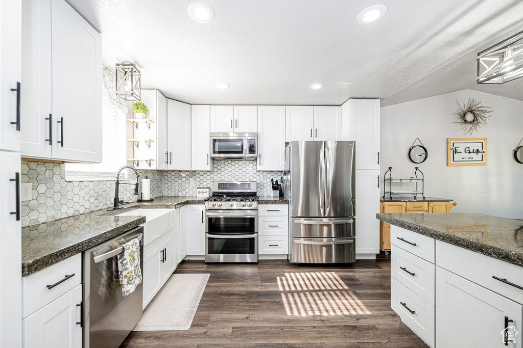 Kitchen featuring stainless steel appliances, backsplash, white cabinets, recessed lighting, and dark stone countertops