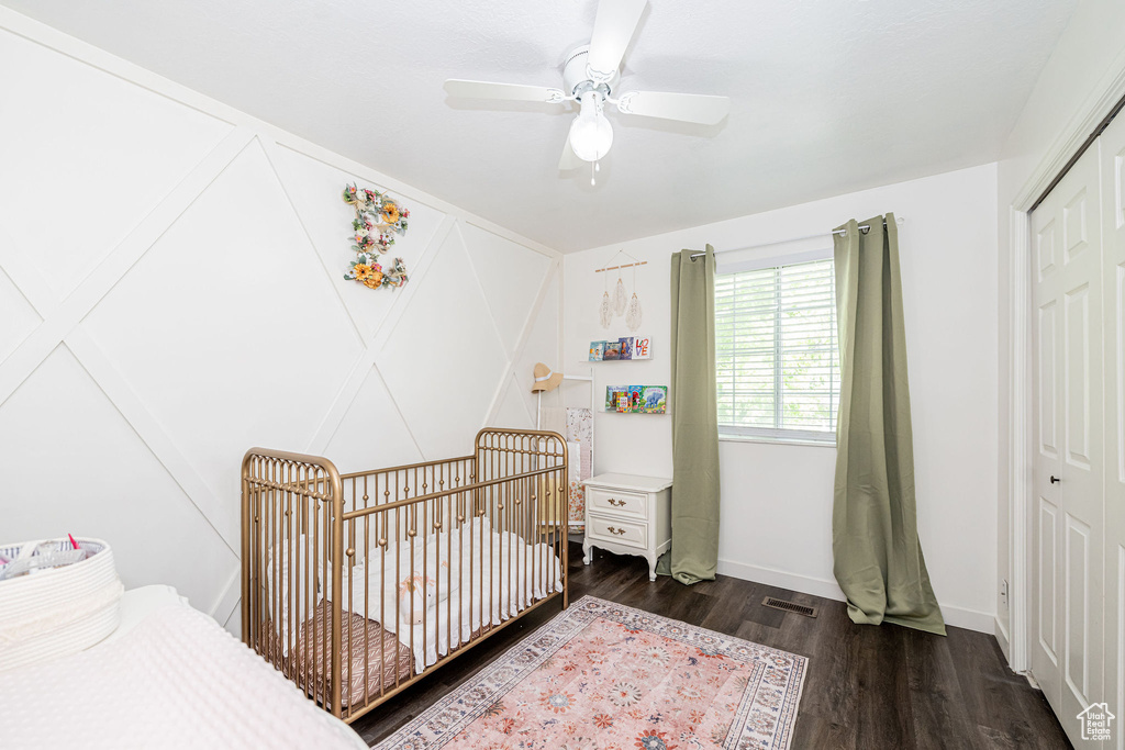 Bedroom with dark wood finished floors, a closet, a nursery area, and a ceiling fan