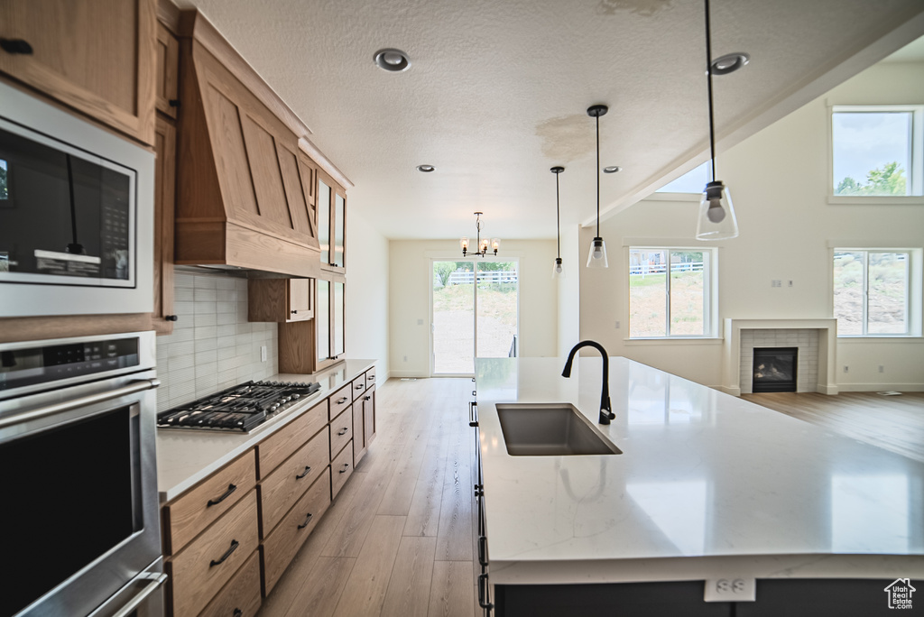 Kitchen featuring appliances with stainless steel finishes, light wood-style floors, premium range hood, brown cabinetry, and recessed lighting