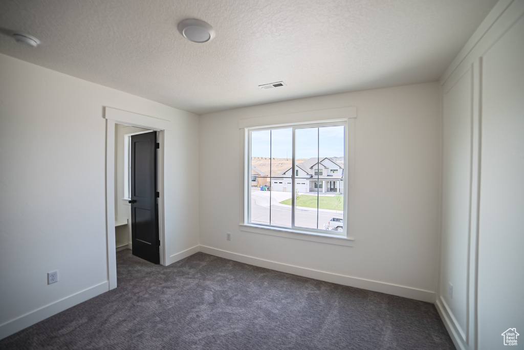Empty room with dark colored carpet, a textured ceiling, and a smoke detector
