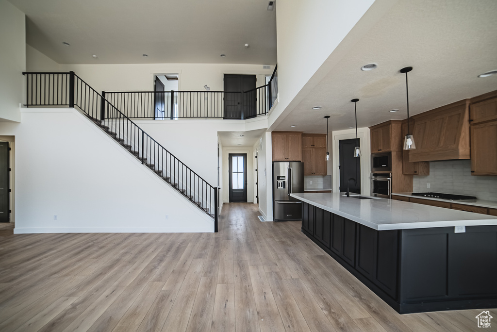 Kitchen with stainless steel appliances, light countertops, brown cabinetry, light wood finished floors, and a high ceiling