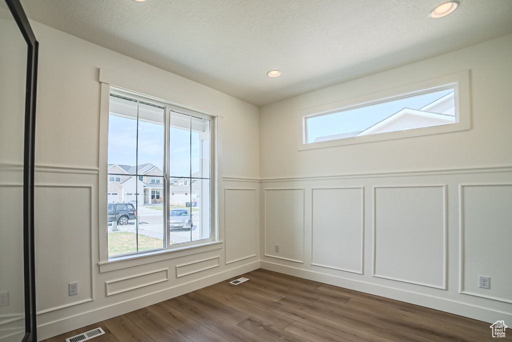 Empty room with a decorative wall, dark wood-style flooring, wainscoting, and recessed lighting