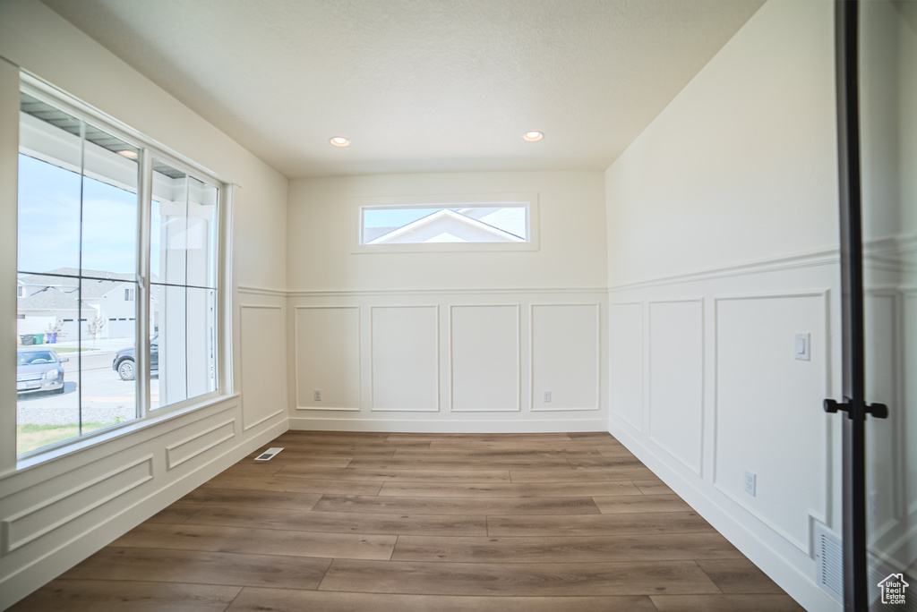 Unfurnished room featuring a decorative wall, healthy amount of natural light, wood finished floors, wainscoting, and recessed lighting