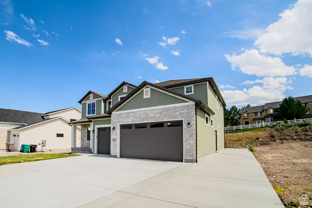 Craftsman-style house featuring stone siding, driveway, and an attached garage