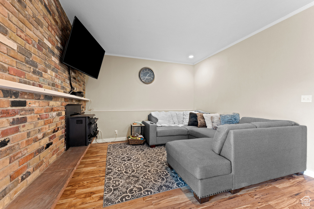 Living area featuring light wood finished floors, a wood stove, crown molding, brick wall, and recessed lighting