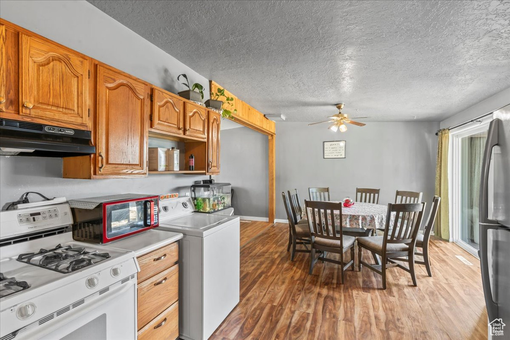 Kitchen with white range with gas stovetop, under cabinet range hood, washer / dryer, light wood-type flooring, and ceiling fan
