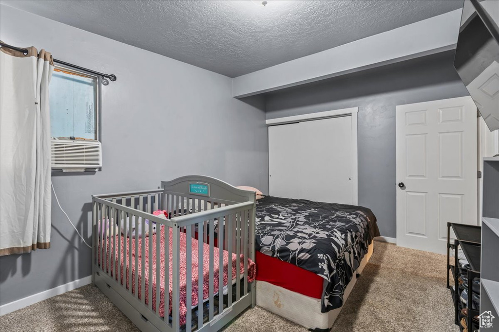 Carpeted bedroom featuring a textured ceiling, cooling unit, and a closet