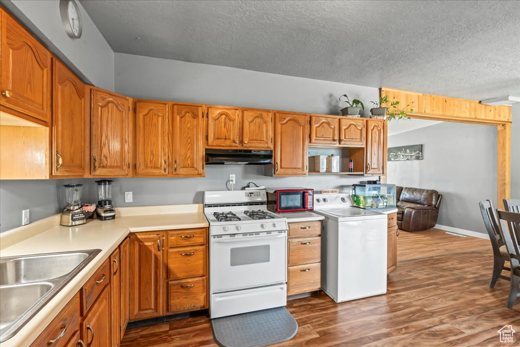Kitchen featuring gas range gas stove, washer / clothes dryer, under cabinet range hood, a textured ceiling, and dark wood finished floors